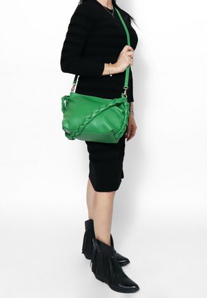 Grüne Leder Schultertasche mit geflochtenem Detail auf der Vorderseite, verstellbarem Tragegurt und glatter Textur. In Crossbody-Style getragen.