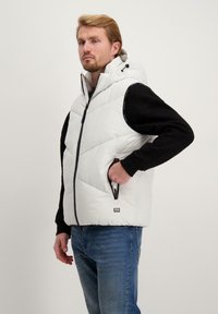 Gevoerde vest met een witte voorkant en zwarte mouwen, voorzien van een hoge kraag, ritssluiting en zijzakken. Soepele textuur en gewatteerd ontwerp.