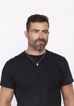 Black cotton t-shirt with short sleeves, round neck, and a silver necklace featuring a small rectangular pendant. Smooth texture.