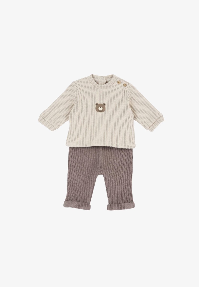 Pull côtelé crème à manches longues avec écusson ours et boutons sur l'épaule, associé à un pantalon côtelé marron avec revers.
