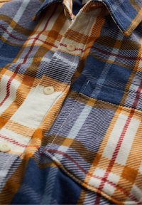 Chemise en flanelle à carreaux avec des couleurs bleu, orange et rouge, dotée d'une fermeture à boutons à l'avant, d'un col et d'une poche poitrine. Tissu doux et texturé.