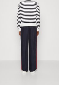 Maglione a righe bianco e blu navy con collo a costine, abbinato a pantaloni blu navy con strisce laterali rosse e vestibilità comoda.