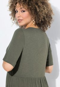 Vestido verde oliva con mangas cortas, un dobladillo acampanado y una textura suave. Presenta un escote redondeado y material acanalado.