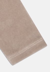 Beżowa aksamitna tkanina o miękkiej teksturze, z wyraźnym brzegiem i subtelnymi przeszyciami wzdłuż krawędzi. Zaokrąglony detal w jednym rogu.