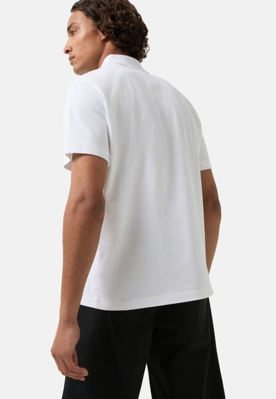 White polo shirt with short sleeves, plain texture, and a classic collar. The back features a straight hemline and minimal design details.