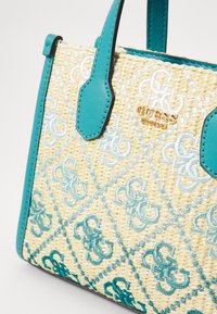 Vævet stråhåndtaske med turkise syntetiske læderdetaljer, prydet med broderede mønstre og et guldlogo på forsiden.