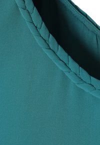 Tela verde azulado con una textura suave que presenta un ribete trenzado en el escote. El diseño enfatiza la simplicidad y un detalle sutil.