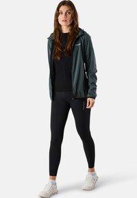 Lightweight, dark green jacket with hood, paired with a black top and black leggings. Athletic shoes complete the outfit.