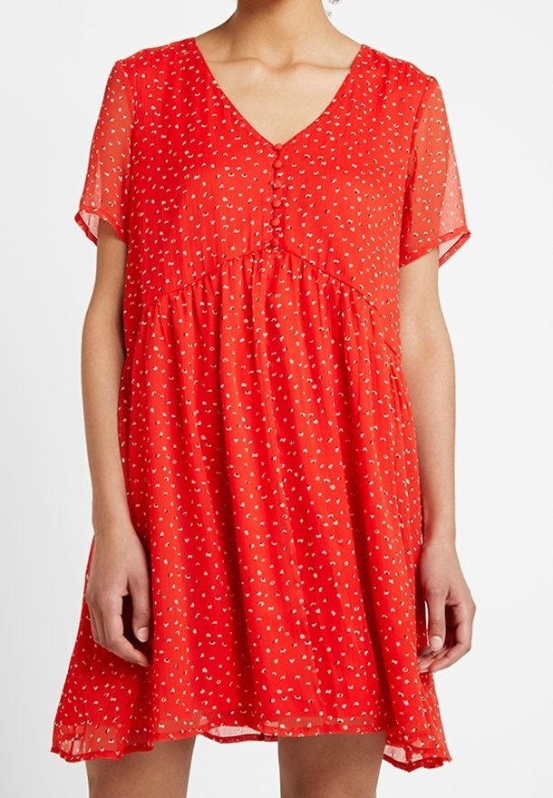 Robe courte rouge à manches courtes avec un col en V, dotée d'une fermeture boutonnée à l'avant, d'une coupe ample, et de motifs à pois blancs sur un tissu transparent.