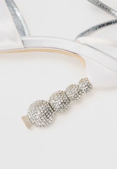Sandalo alto argento con cinturini in satin, dettagli metallici e un tacco decorativo ricoperto di cristalli con tre elementi sferici.