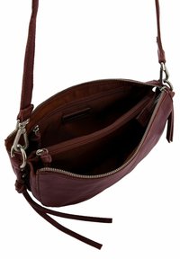 Sac bandoulière en cuir bordeaux foncé avec une sangle texturée, deux compartiments zippés et un détail de pompon décoratif. Accents en métal argenté.