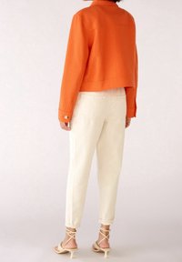 Orange strukturerad kort jacka med två knappar, kombinerad med krämfärgade avsmalnande byxor och beige sandaletter med klackar. Rena linjer och enkel design.