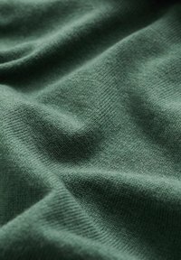 Mörkgrön tyg med en slät yta, som uppvisar subtila ribbningar och veck, vilket indikerar ett mjukt, stretchigt material som är lämpligt för kläder.