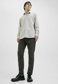 Cămașă cu dungi, cu mânecă lungă și guler butonat, împerecheată cu pantaloni subțiri de culoare verde închis și pantofi negri cu șireturi. Texturi netede.