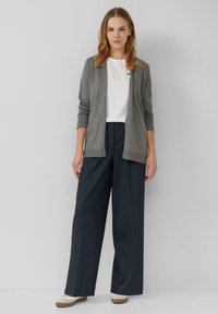 Grijze lange mouw cardigan over een wit T-shirt, gecombineerd met donkere, rechte broek en beige schoenen. Eenvoudig ontwerp met een klassieke pasvorm.