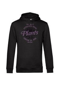 Felpa nera con cappuccio caratterizzata da una grafica centrale con il testo "Le piante più interessanti crescono all'ombra" in viola, accompagnata da un design floreale.