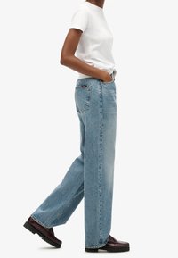 Vaaleansiniset deniminiityt rentolla istuvuudella, suora lahjemalli ja minimaalinen yksityiskohtaisuus. Yhdistetty yksinkertaiseen valkoiseen t-paitaan ja tummiin kenkiin.