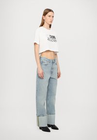 Balta trumpa marškinėliai su juodu užrašu "CHINO JEANS". Šviesiai mėlynos, aukštai įsitaisiusios tiesaus kirpimo džinsai su surišamais rankogaliais. Juodi vidutinio aukščio auliniai batai.