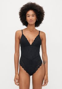 Fekete csipkebodysuit állítható spagettipántokkal, mély dekoltázzsal, virágmintával és hullámos szegéllyel.