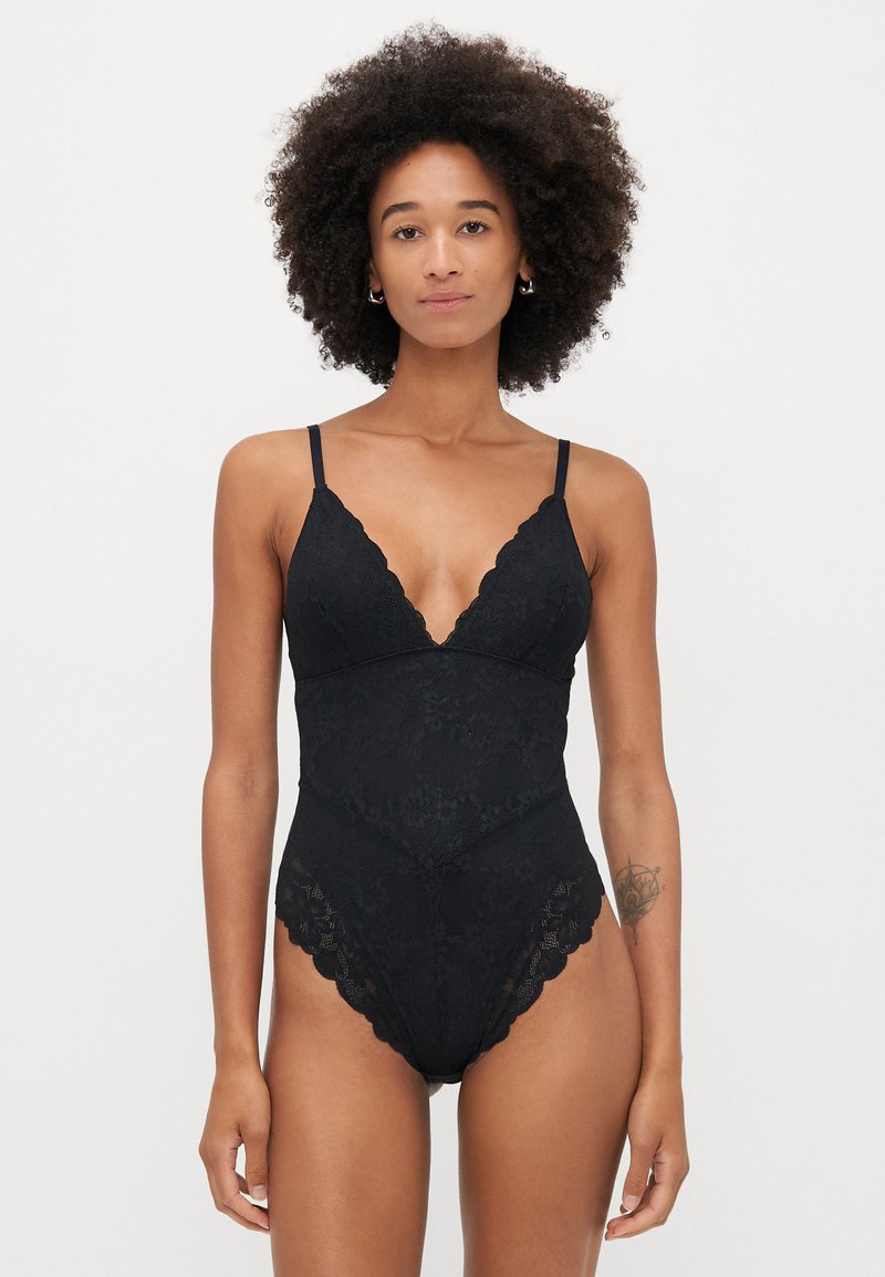 Fekete csipkebodysuit állítható spagettipántokkal, mély dekoltázzsal, virágmintával és hullámos szegéllyel.