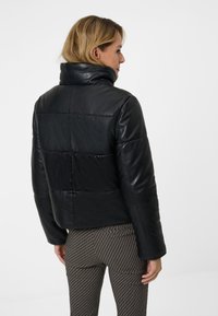 Svart läderkort jacka med hög krage, med quiltad design och slät finish, bärs med mönstrade byxor.