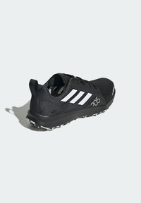 Scarpa sportiva nera con tomaia texture, design a tre strisce bianche e un numero "205" bianco in contrasto sul lato. Suola in gomma con tacchetti.