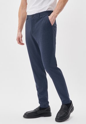 Pantaloni navy slim-fit realizzati in tessuto morbido, dotati di tasche laterali, chiusura con un pulsante e una trama sottile. Abbinati a mocassini neri.