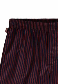 Pantalons de pyjama rayés en bordeaux et bleu marine, avec une taille élastique et une petite étiquette de marque sur le côté. Tissu doux et lisse.