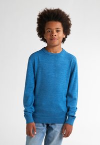 Maglione azzurro a maniche lunghe con scollatura rotonda, polsi e orlo a coste, e texture liscia. Indossato con jeans in denim azzurro chiaro.