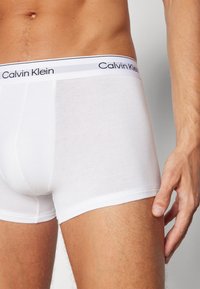Hvite bomullsboxere med myk tekstur, med en elastisk midjeinnsats i svart og grått, tettsittende design og glatte sidesømmer.