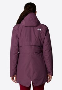 Veste étanche violette avec capuche et taille réglable, dotée d'une aération dans le dos et d'un logo sur le haut du dos. Texture lisse, manches longues.