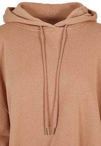 Heled roosa kapuutsiga särk, mis on valmistatud pehmest kangast, millel on V-kaeluse disain, reguleeritav pael metalltipudega ja lõdvendatud istuvus.