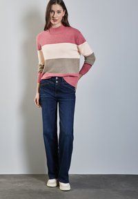Stickad tröja med rosa, krämfärgade och grå horisontella ränder, med en hög krage. Kombinerad med mörkblå utsvängda jeans och ljusa sneakers.