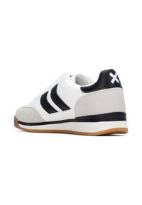 Zapatilla blanca con rayas negras, detalles de gamuza gris y una suela de goma de color natural. Cuenta con un cuello acolchado y una superficie texturizada para un mejor agarre.