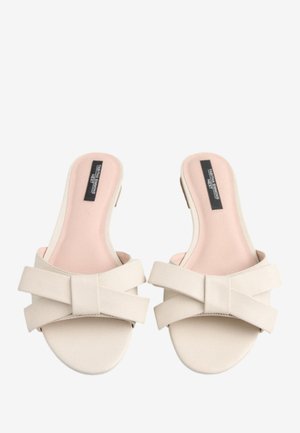 Beige Slide-Sandalen mit einer glatten Kunstleder-Oberfläche, ausgestattet mit einem breiten Kreuzriemen mit Schleifendetail und einer weichen rosa Innensohle.