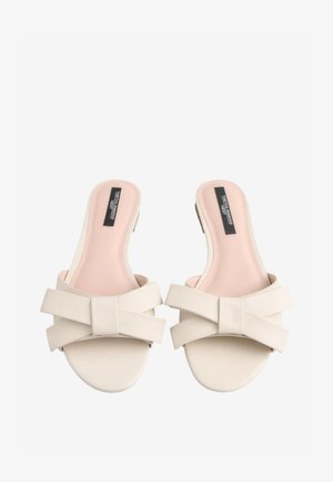 Beige slippers met een gladde faux lederen afwerking, uitgerust met een brede gekruiste band met een strikdetail en een zachtroze binnenzool.