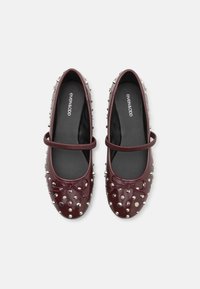 Ballerines en cuir bordeaux avec des accents cloutés, bout rond et un nœud décoratif avec une bride à la cheville. Texture lisse et design élégant.