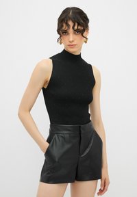 Top nero a costine senza maniche con collo alto, decorato con piccoli rivetti argentati. Abbinato a pantaloni corti in ecopelle neri a vita alta.