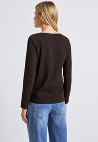 Brauner, gerippten Langarm-Oberteil mit schmalem Rückenausschnitt und geradem Saum, kombiniert mit hellblauen, locker sitzenden Jeans.