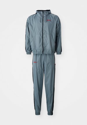 Grijze hoodie met een ritssluiting aan de voorkant en zwarte accenten, gecombineerd met bijpassende broek met elastische boorden en een slim fit. Rode logodetail.
