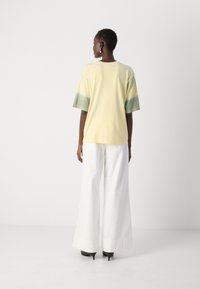 Cotton t-shirt in pale yellow with green and beige gradient short sleeves. Paired with white wide-leg trousers and black high heels.