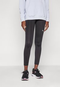 Leggings sportivi neri con una texture liscia, dotati di un logo PUMA. Abbinati a una felpa leggera blu e a scarpe nere con dettagli rosa.