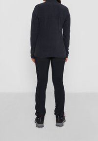 Mustat fleece-takit, joissa on korkea kaulus, yhdistettyinä mustiin slim fit -housuihin. Molemmissa on sileä pinta ja ne on suunniteltu lämpimiksi.