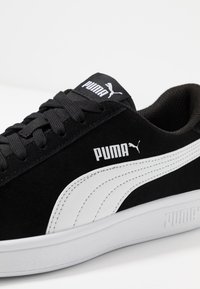 Baskets en daim noir avec des accents blancs, présentant une tige texturée, un bout rond, des lacets plats et une marque "PUMA" en relief sur le côté.