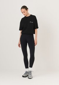 Fekete, oversized póló hímzett logóval, fekete leggingsszel, fehér zoknikkal és ezüst színű futócipőkkel párosítva. Lapos, sima szövettextúrák.