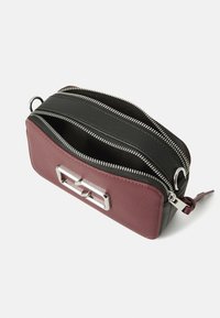 Sac rectangulaire à double compartiment en cuir bordeaux et noir. Doté de fermetures éclair en métal argenté, d'accessoires en métal et d'une petite languette.
