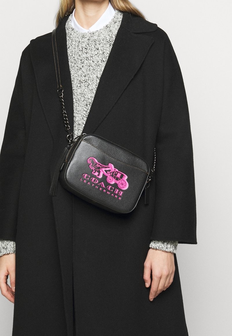 Schwarze Leder-Umhängetasche mit strukturierter Oberfläche, ausgestattet mit rosa grafischen Designs und einem Quasten, ergänzt durch einen Metallkette-Trageriemen.