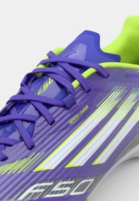 Scarpa da calcio indoor viola con dettagli in verde neon, tomaia sintetica texturizzata, lacci viola e strisce bianche. Presenta il marchio "F50".