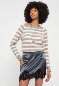 Dryžuotas smėlio ir kreminės spalvos megztinis su ilgomis rankovėmis, derinamas su pilku satino sijonu su juodos nėriniuotos apdailos detalėmis. Sidabrinė širdies formos pakabuko vėrinys.