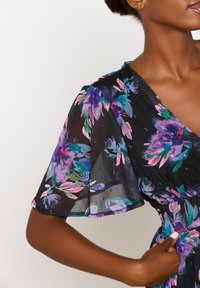 Svart blommig klänning med korta fladdrande ärmar, prydd med livfulla lila, rosa och gröna blommor. Lätt, genomskinlig tyg med en subtil textur.